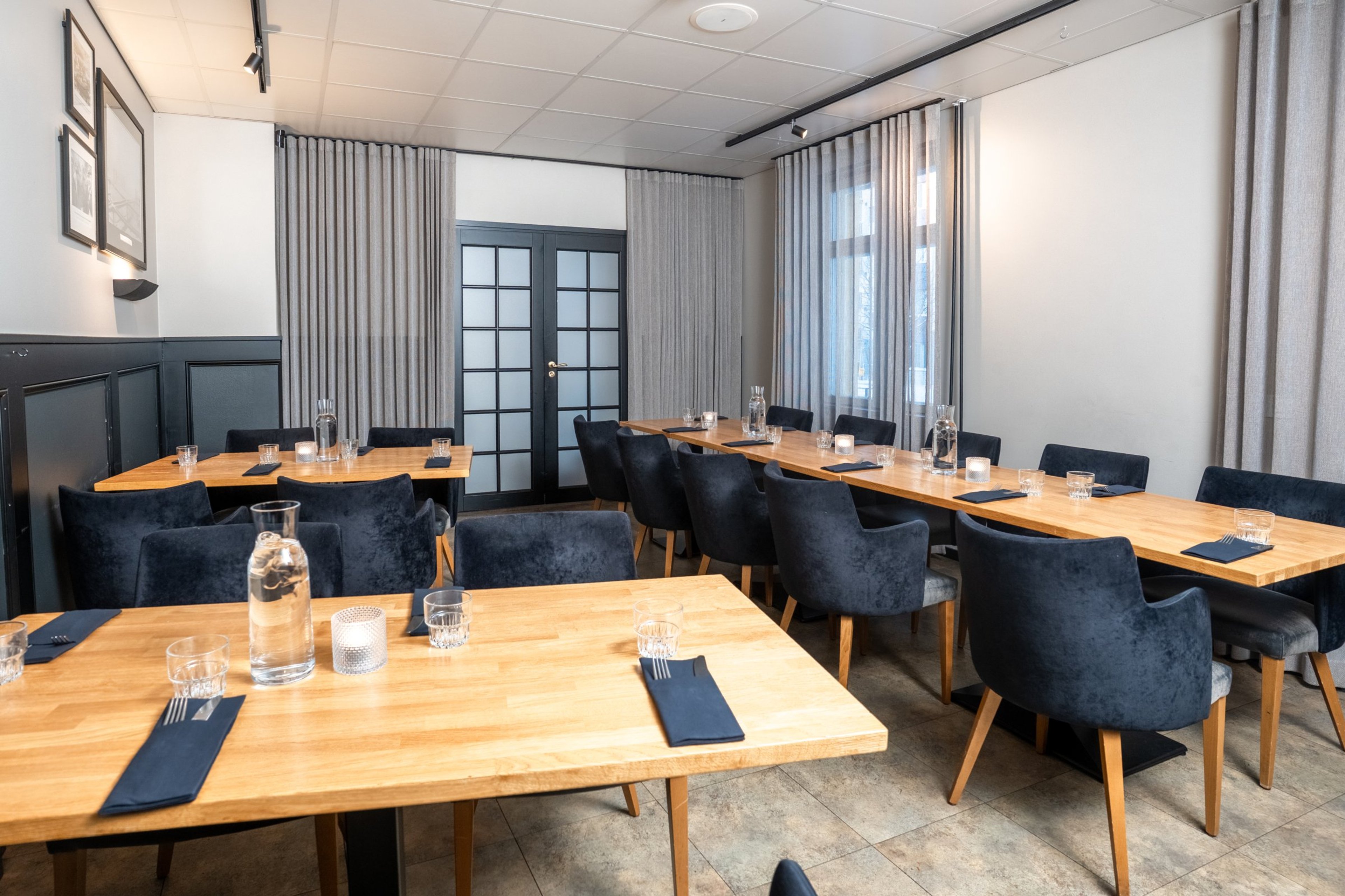 Kokoustila puisilla pöydillä ja tummansinisillä tuoleilla. Tila on valoisa, lattialla kivilaattoja ja seinillä vaaleat verhot.