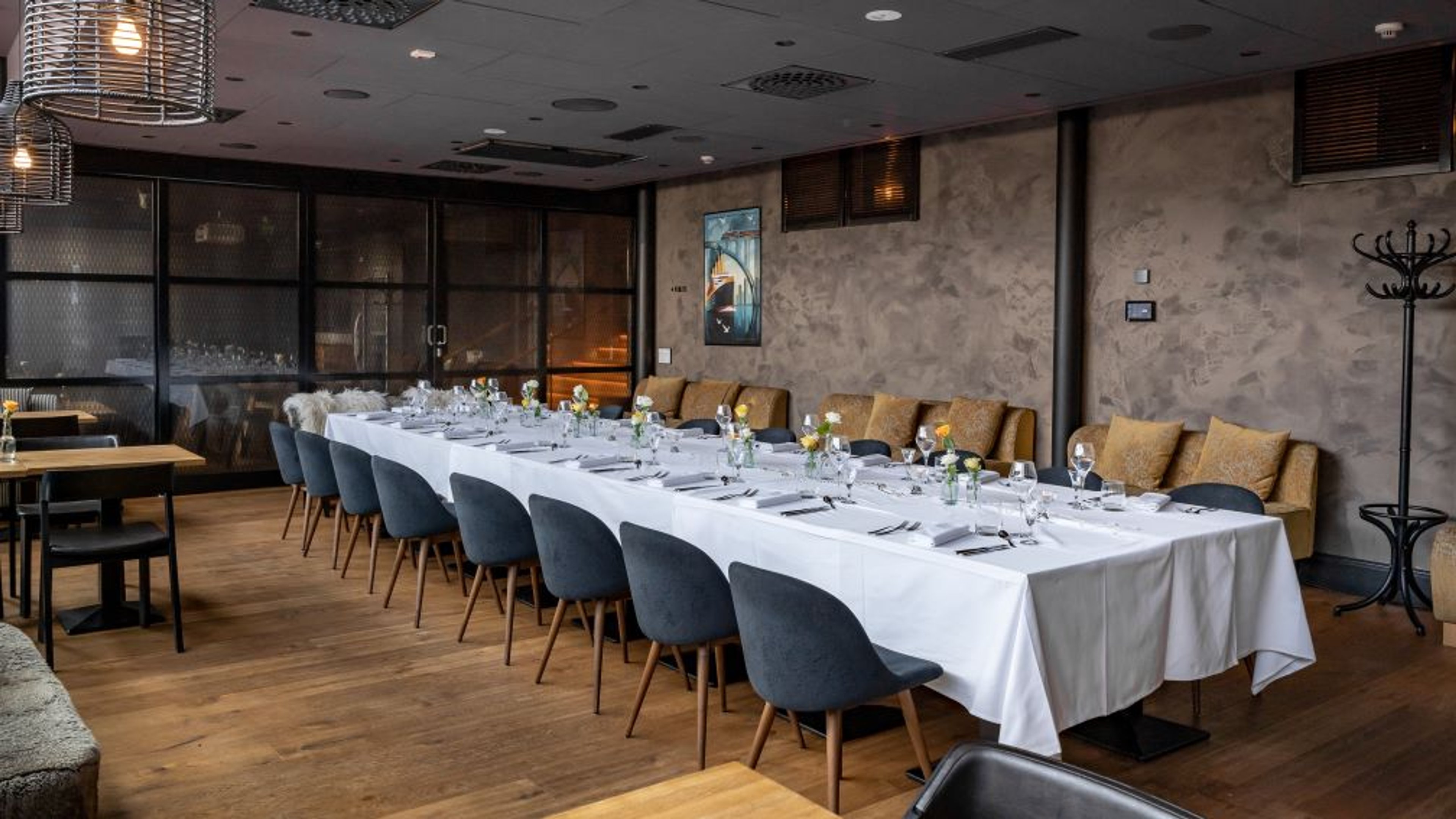 Ravintolan tyylikäs yksityistila pitkällä pöydällä, sinisillä tuoleilla ja puulattialla. Seinillä on teksturoitu pintakäsittely ja naulakko.