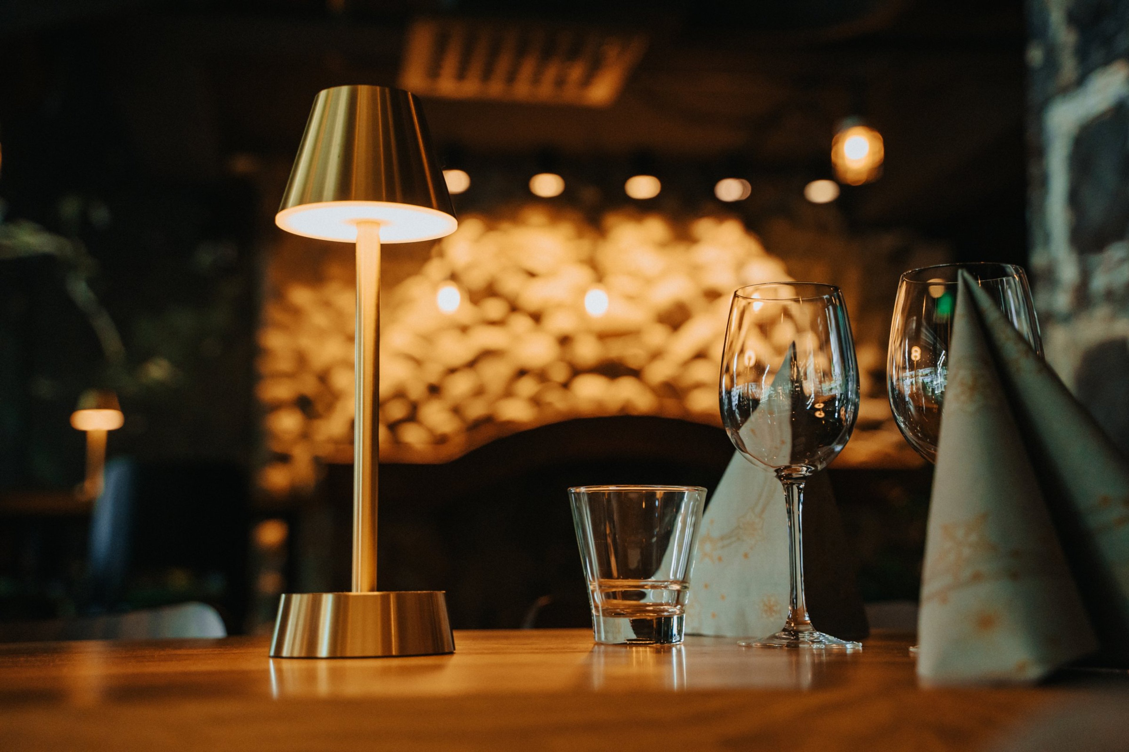 Ravintolan pöytä jossa messinkinen pöytävalaisin, tyhjä lasi ja viinilaseja.