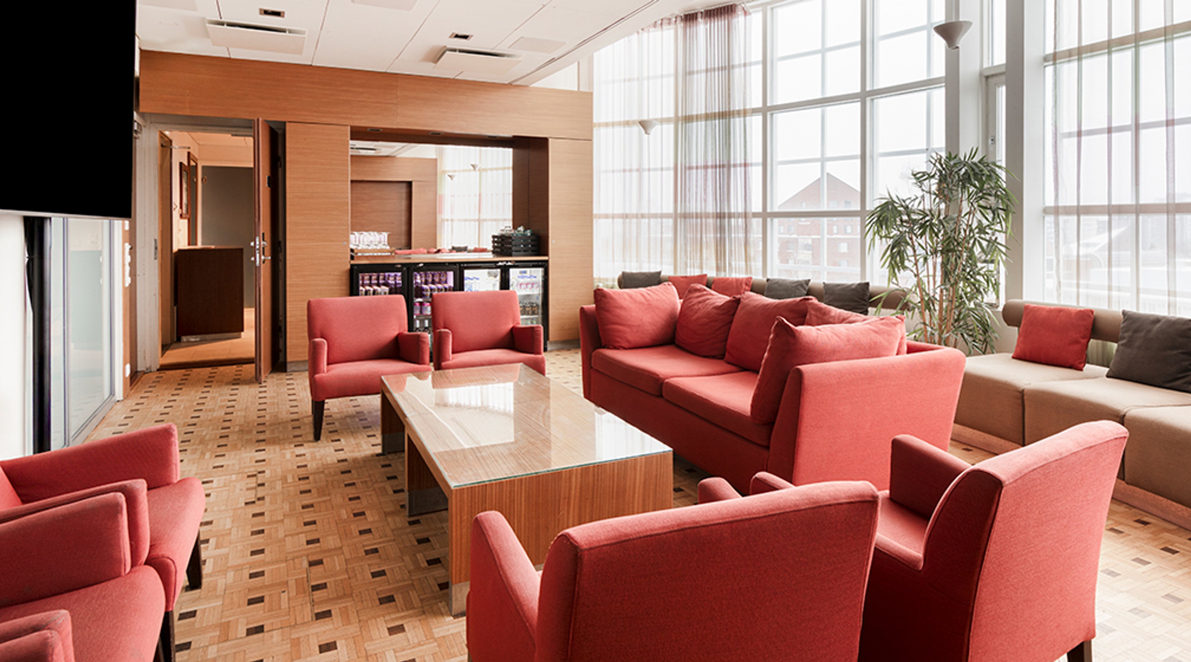 Valoisa oleskelutila, jossa punaiset sohvat ja nojatuolit puisen pöydän ympärillä. Taustalla isot ikkunat ja palvelutiski.