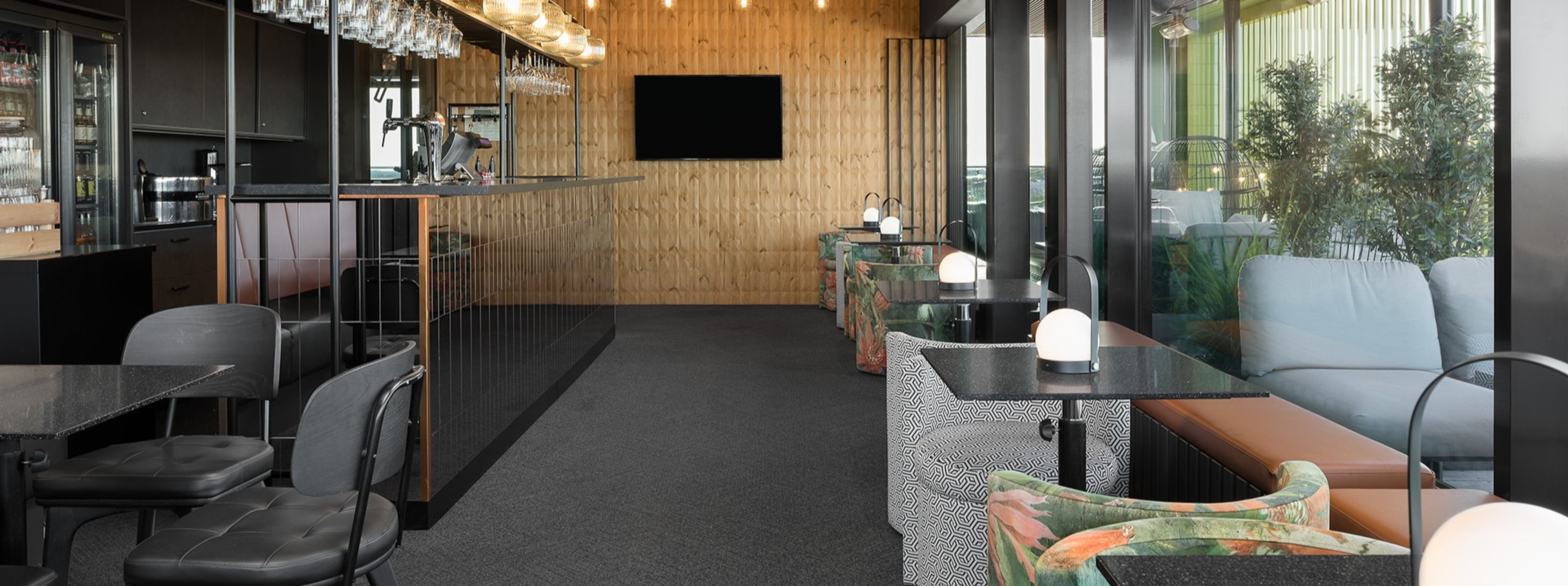 Moderni loungealue puupaneeliseinillä, baaritiskillä ja istuinryhmillä. Tasainen lattiapinta, hyvä valaistus ja leveät kulkuväylät.