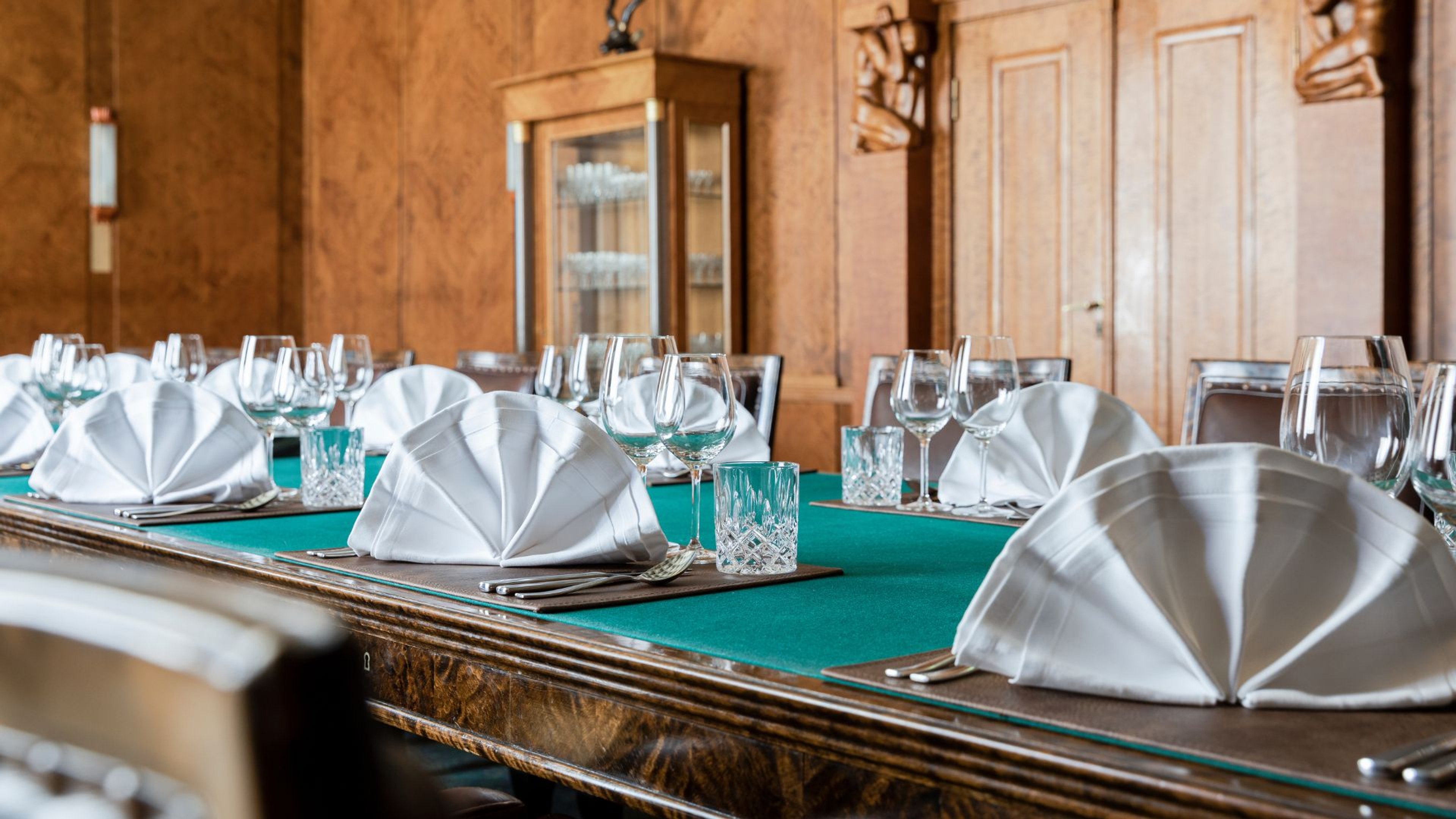 Elegantisti katettu pöytä ravintolassa, jossa taitellut valkoiset lautasliinat, kristallilasit ja turkoosi pöytäliina puisella pöydällä.