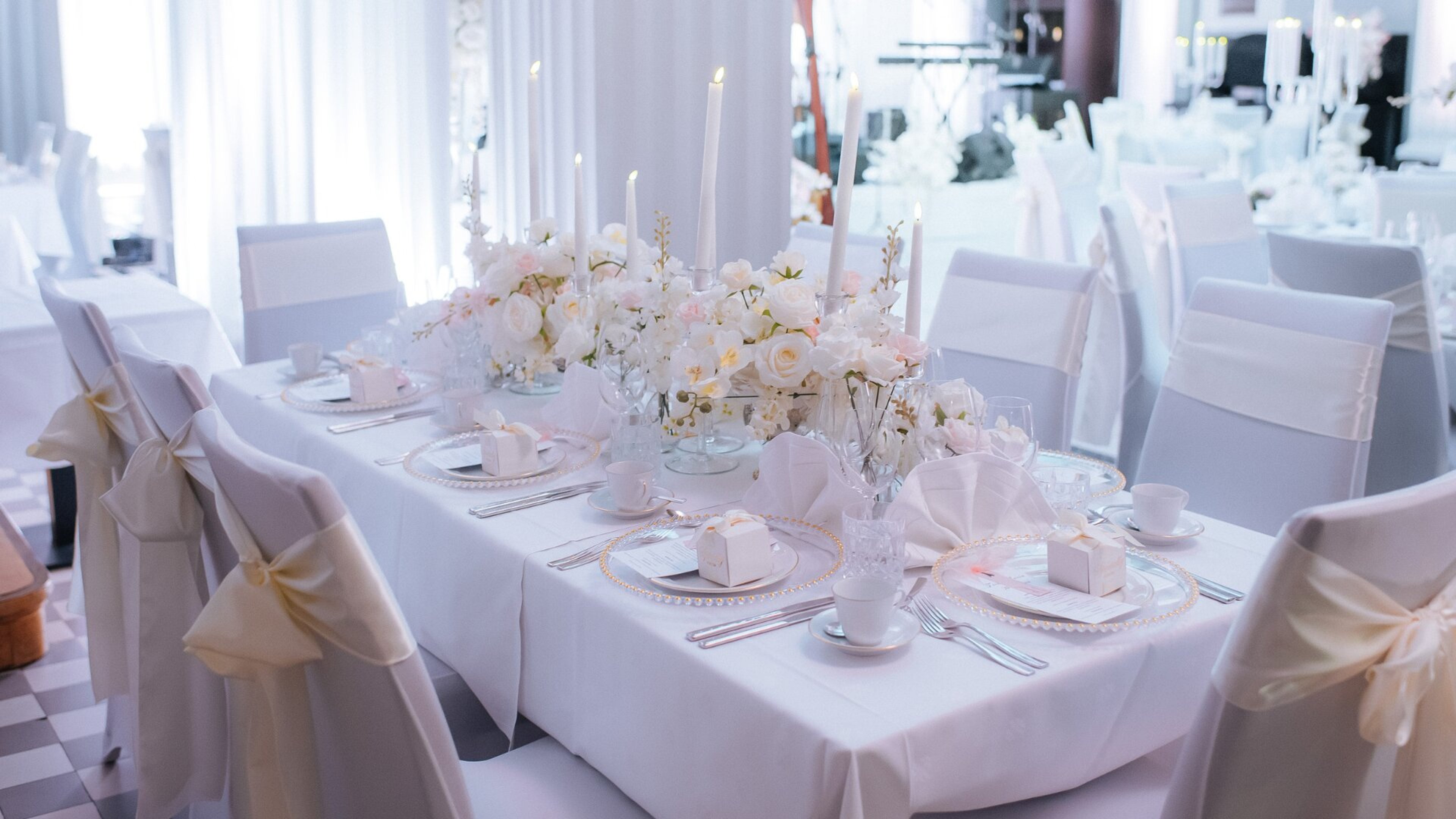 Elegantne valge pulmapidulaud lillekaunistuste, küünalde ja stiilse lauaserveeringuga. Avar laud valgete toolidega.