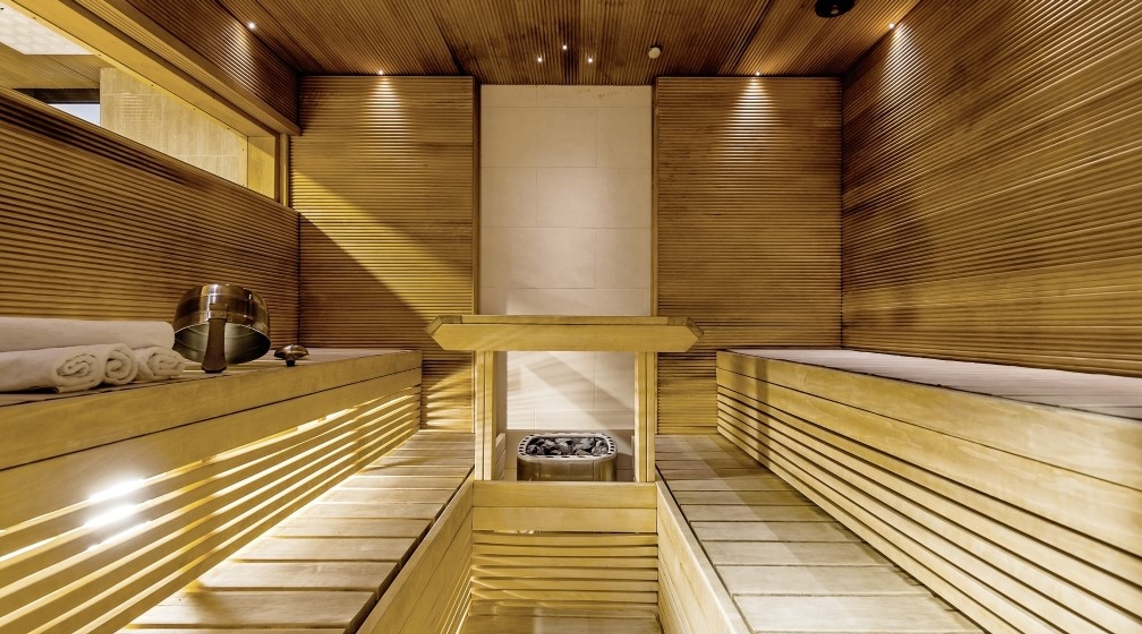 Moderni puusauna vaalein puupaneelein, seinillä ja katossa. Pitkät lauteet molemmilla sivuilla ja kiuas keskellä.