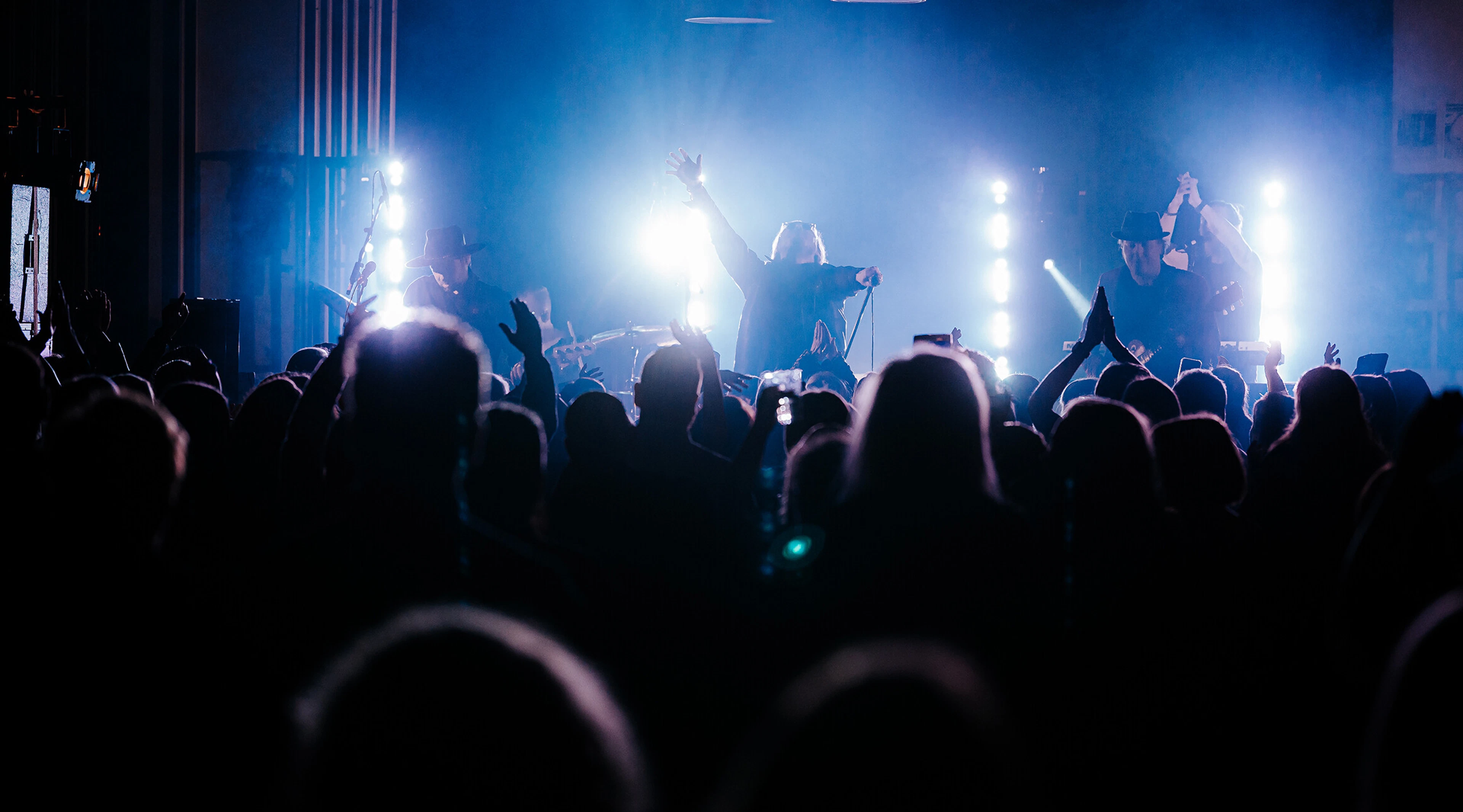 Concert in a packed venue. Audience stands in front of the stage amid blue lighting.