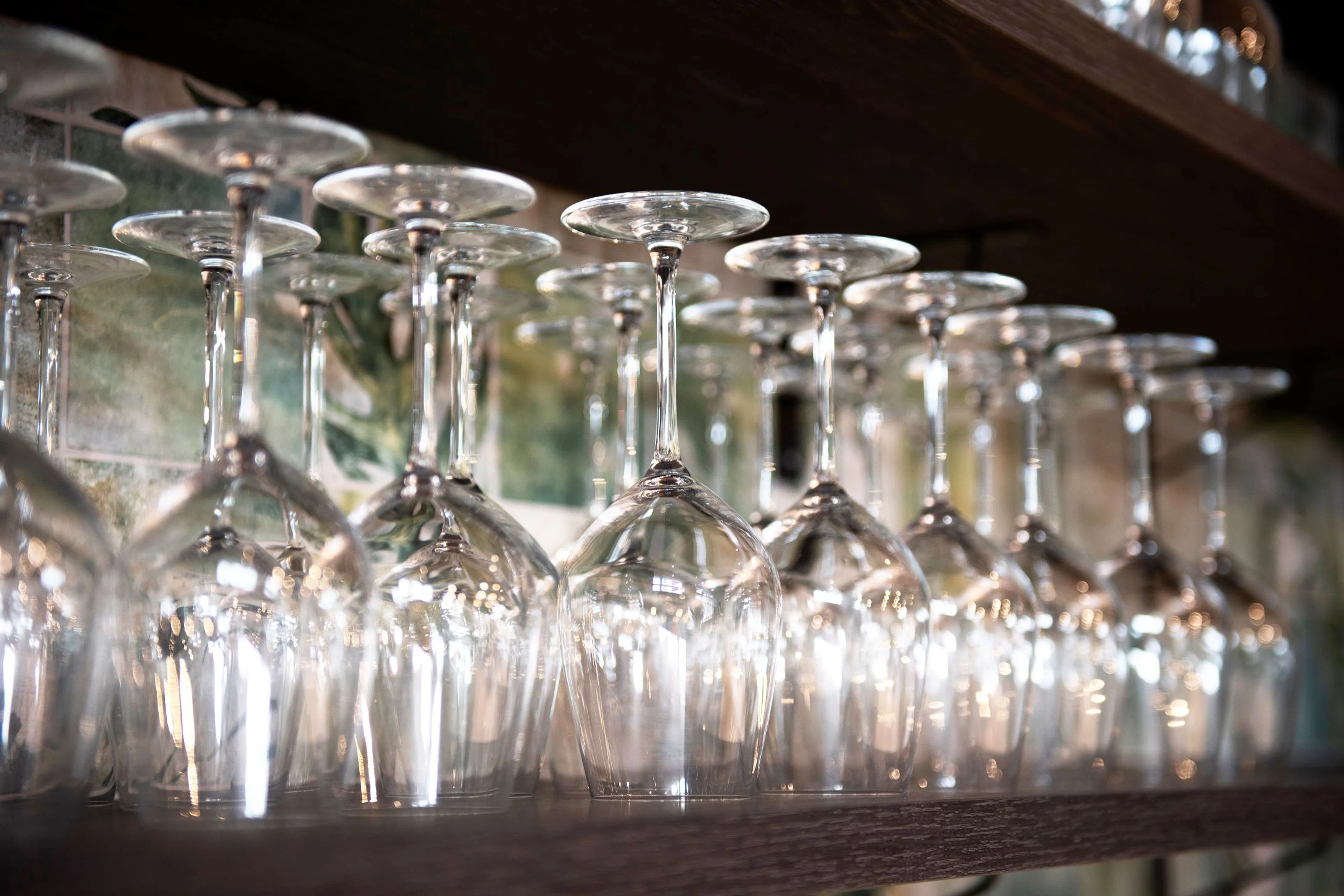 Row of upside-down wine glasses on a shelf, glasses sparkling in the light.