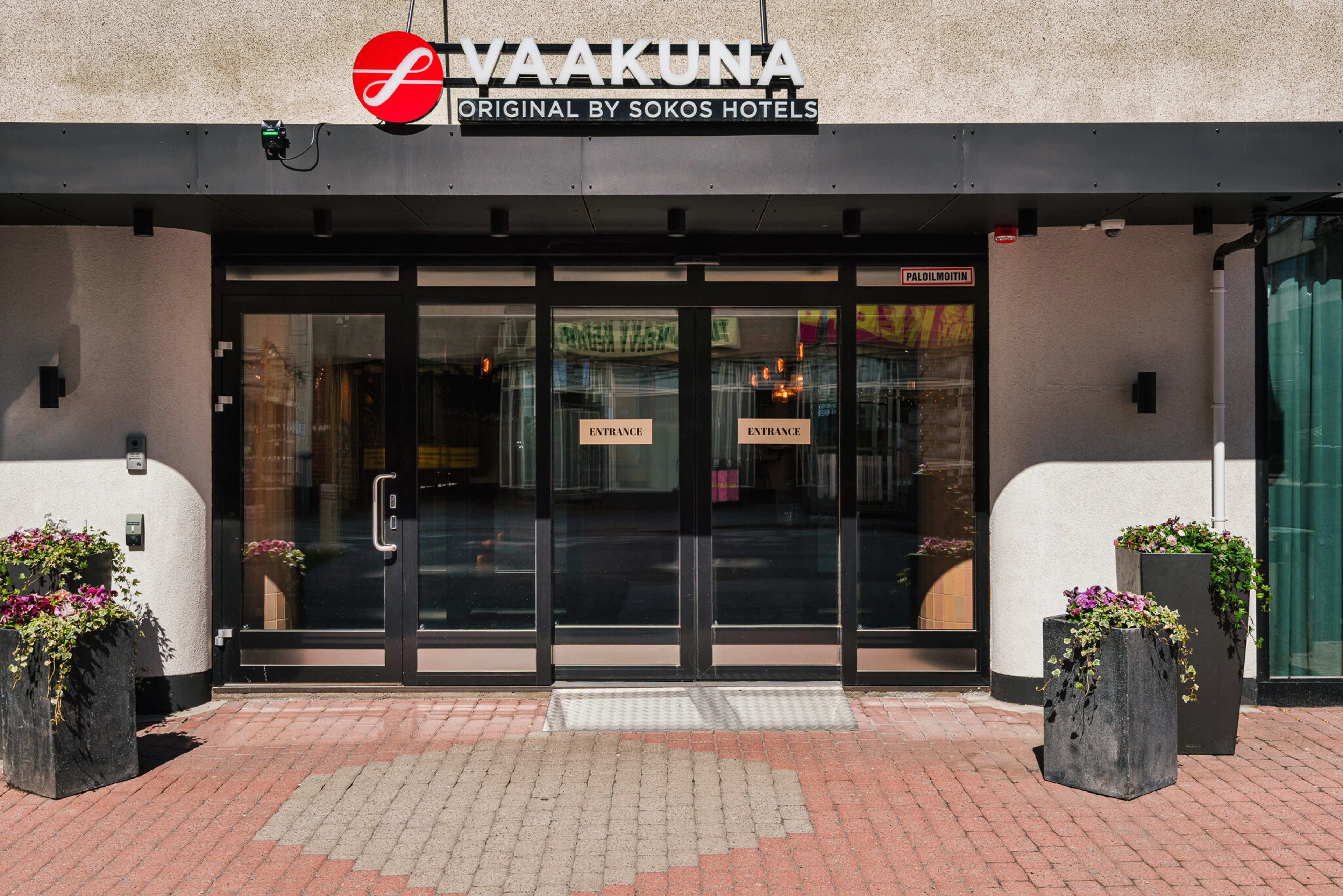 Hotel main entrance with wide dark-framed glass doors, step-free access, and paved brick entry area.