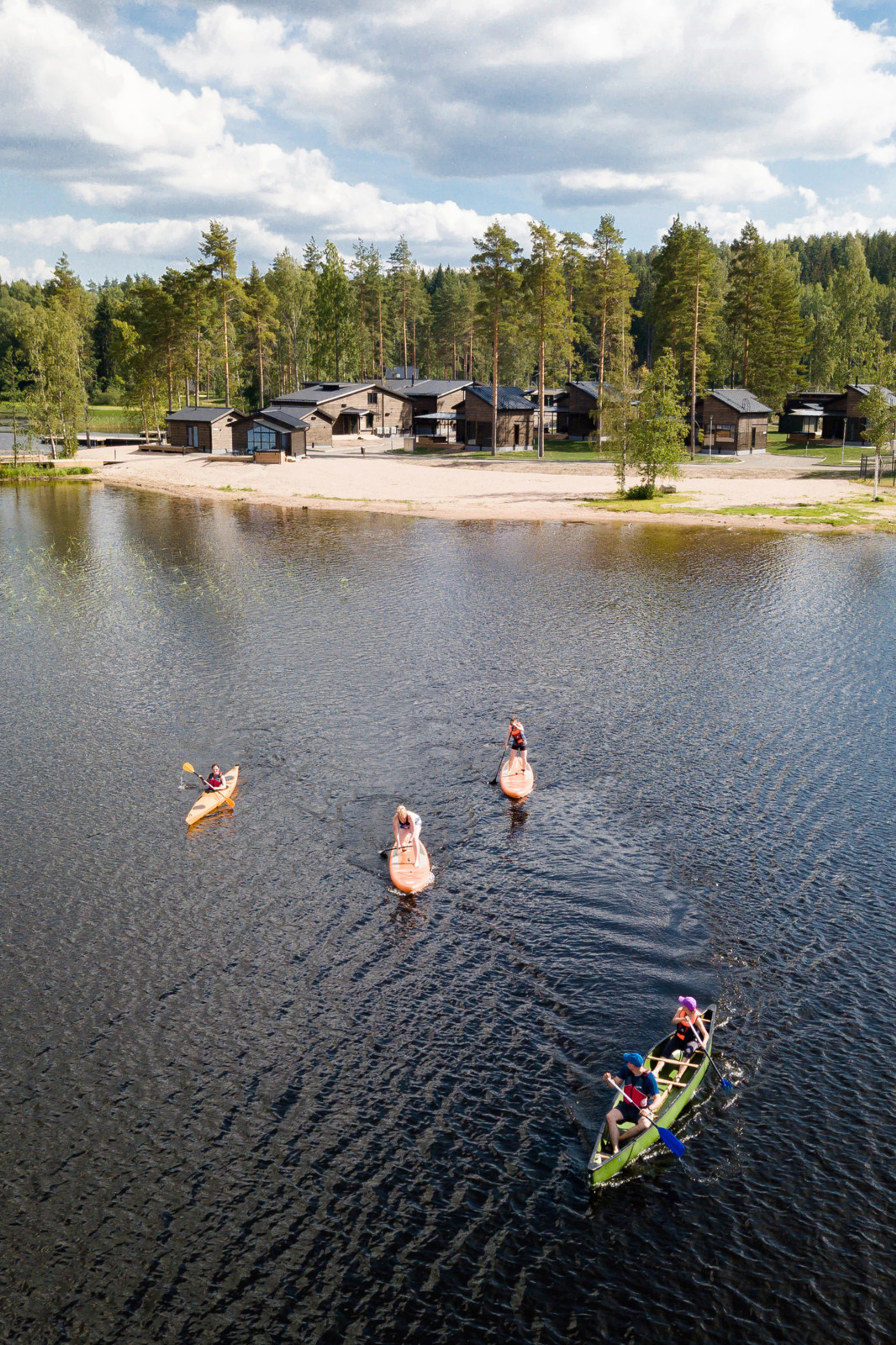 Ihmisiä meloo ja sup-lautailee järvellä. Taustalla näkyy resortalue.