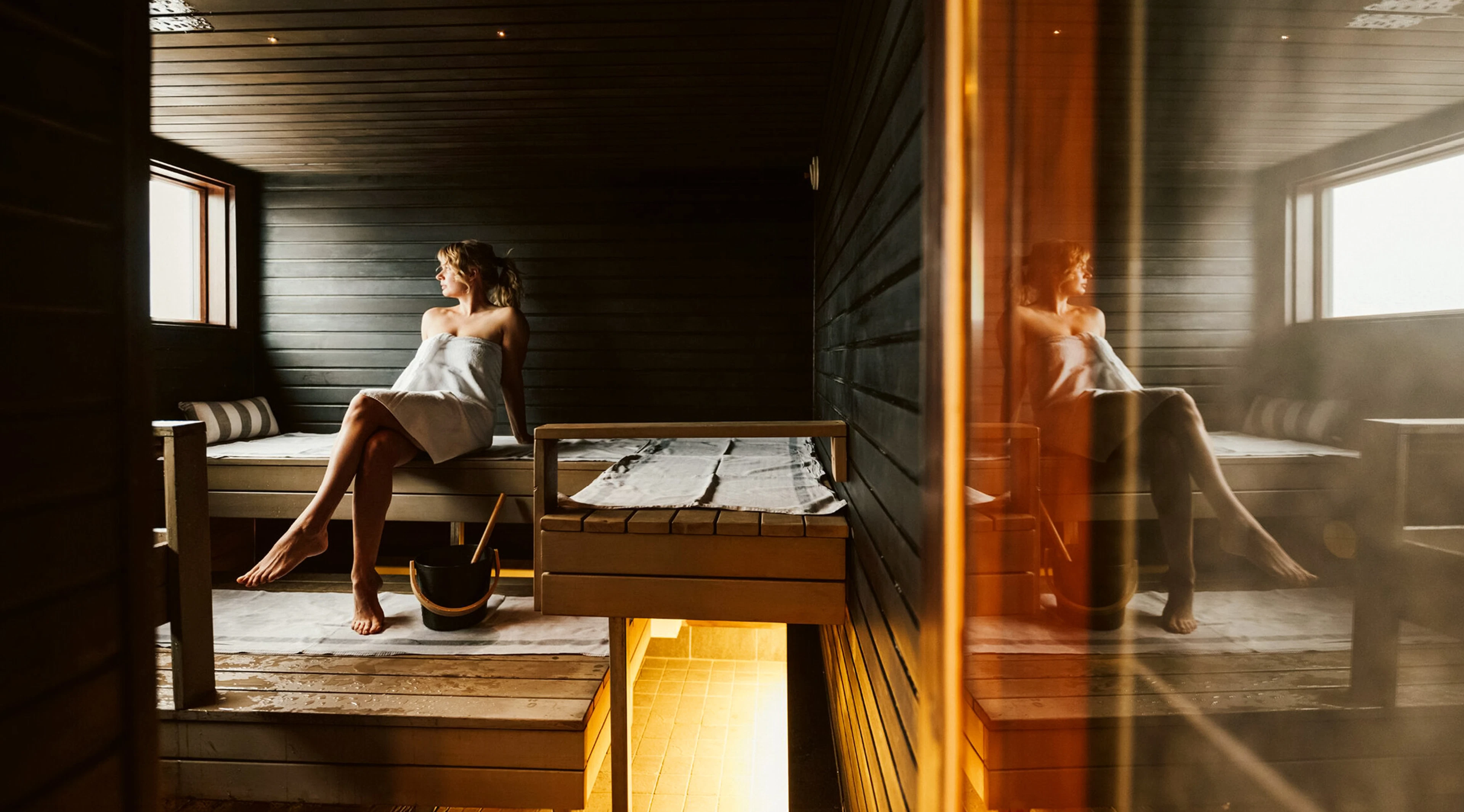 Sauna, jossa puupaneelit, lauteita eri tasoilla ja pehmeää luonnonvaloa ikkunoista.