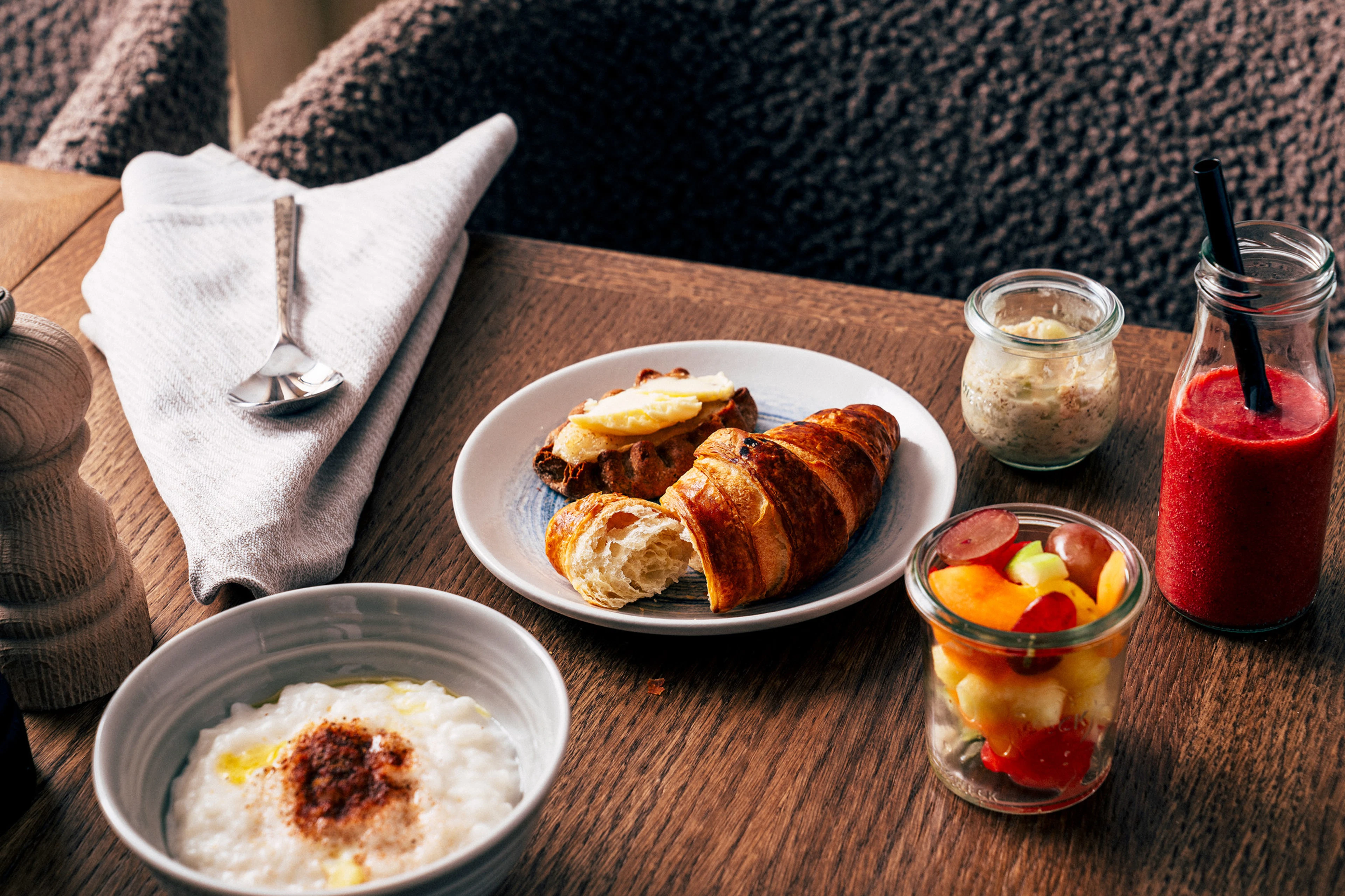 Ett hotellfrukostbord med en skål gröt, croissant och Karelska pirog, frukt och smoothie.
