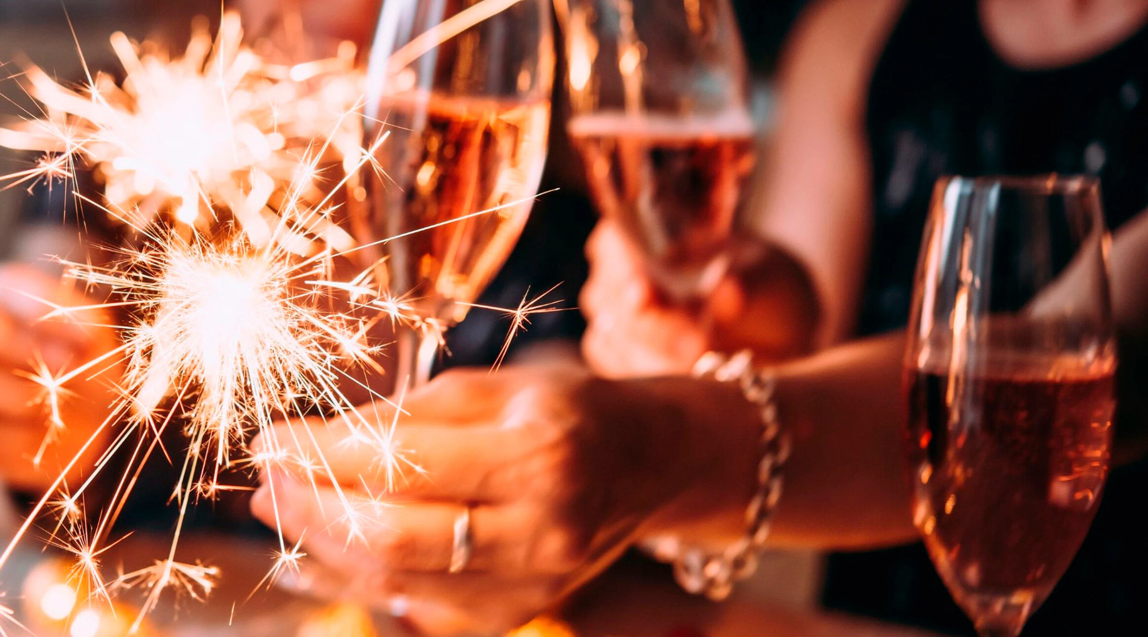 People celebrating with champagne glasses and lit sparklers.