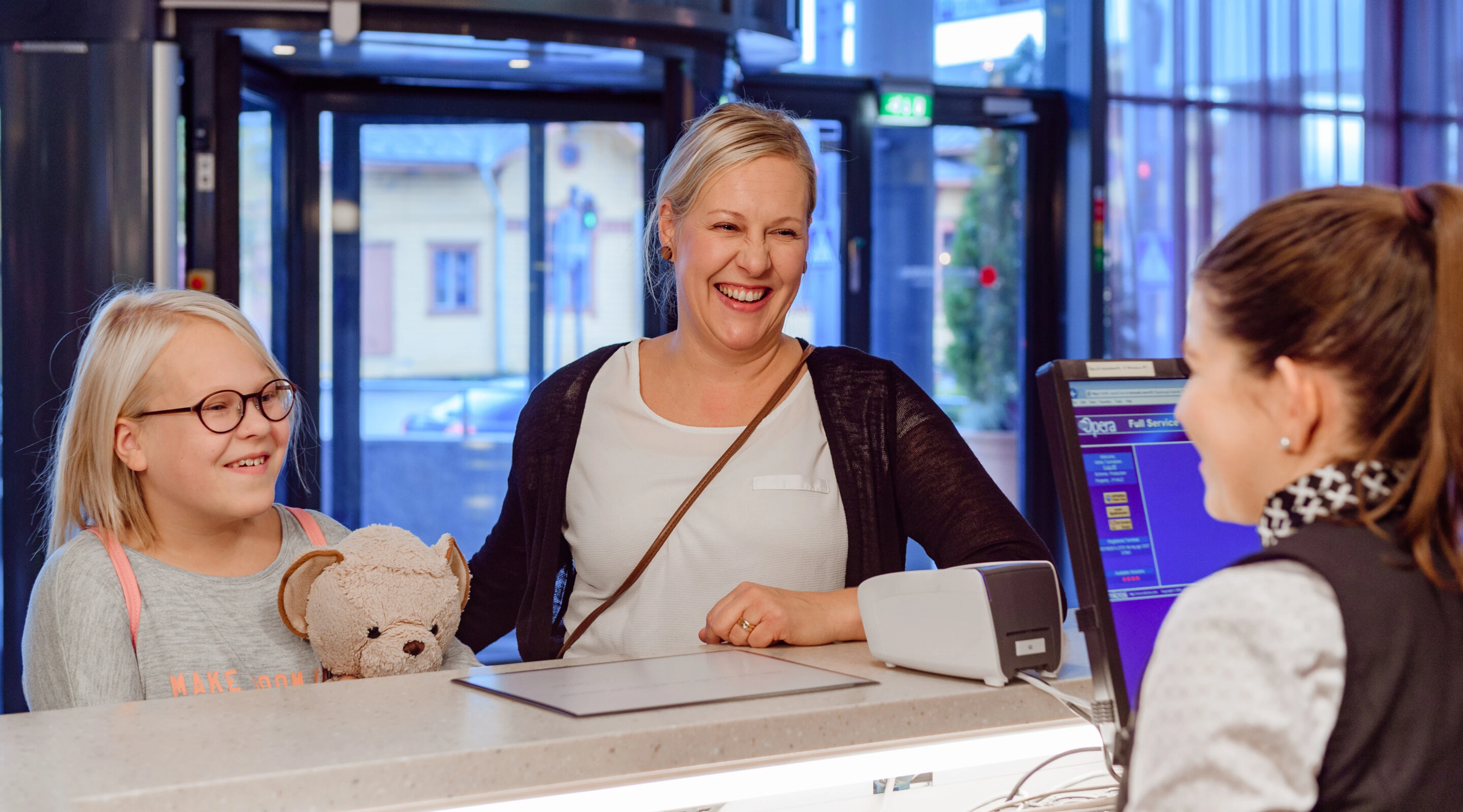 Vastaanottotiski, jossa asiakas asioi työntekijän kanssa. Laajan lasioven kautta näkyy ulkoalueelle.