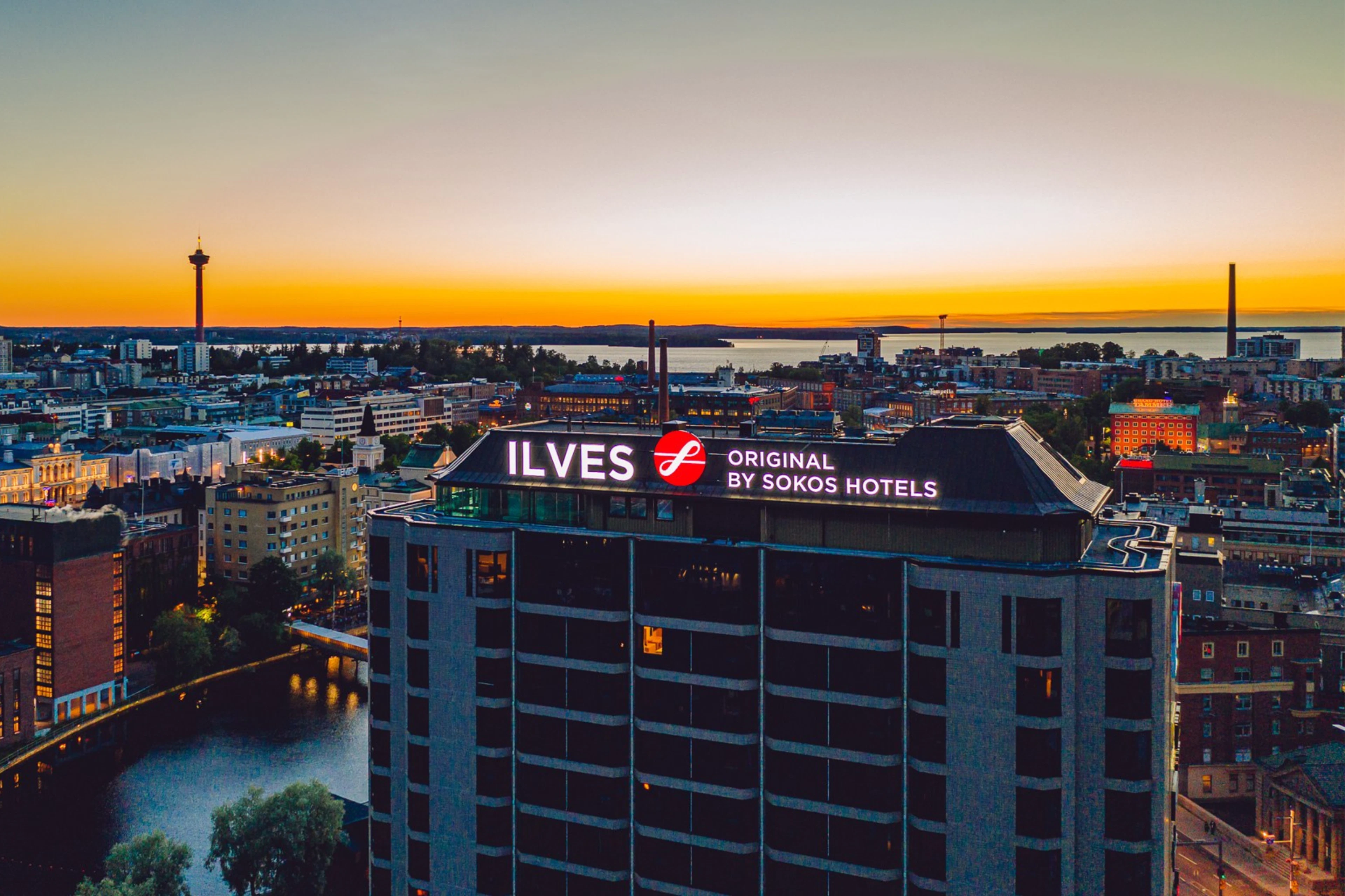 Ilmakuva Original Sokos Hotel Ilveksestä ja Tampereen keskustasta auringonlaskun aikaan. Etualalla Ilves-hotelli, taustalla näkyy Näsinneula ja järvimaisemaa.