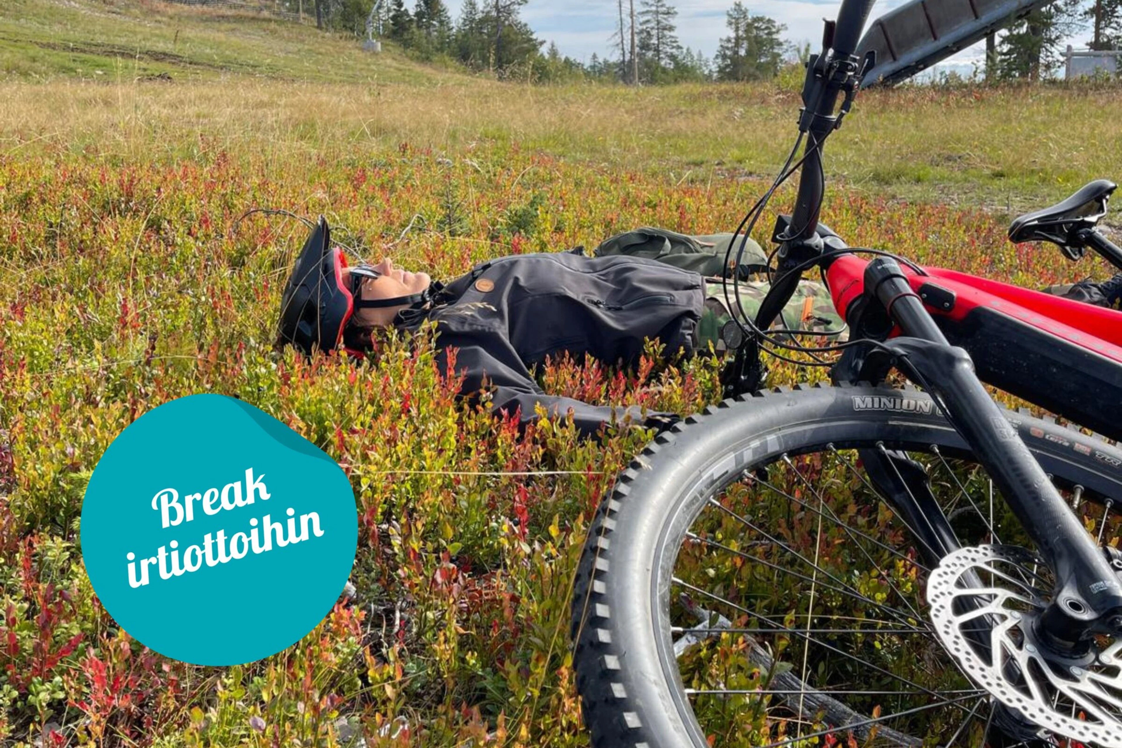 Person resting on the ground beside a mountain bike among colourful autumn vegetation in a forest setting.