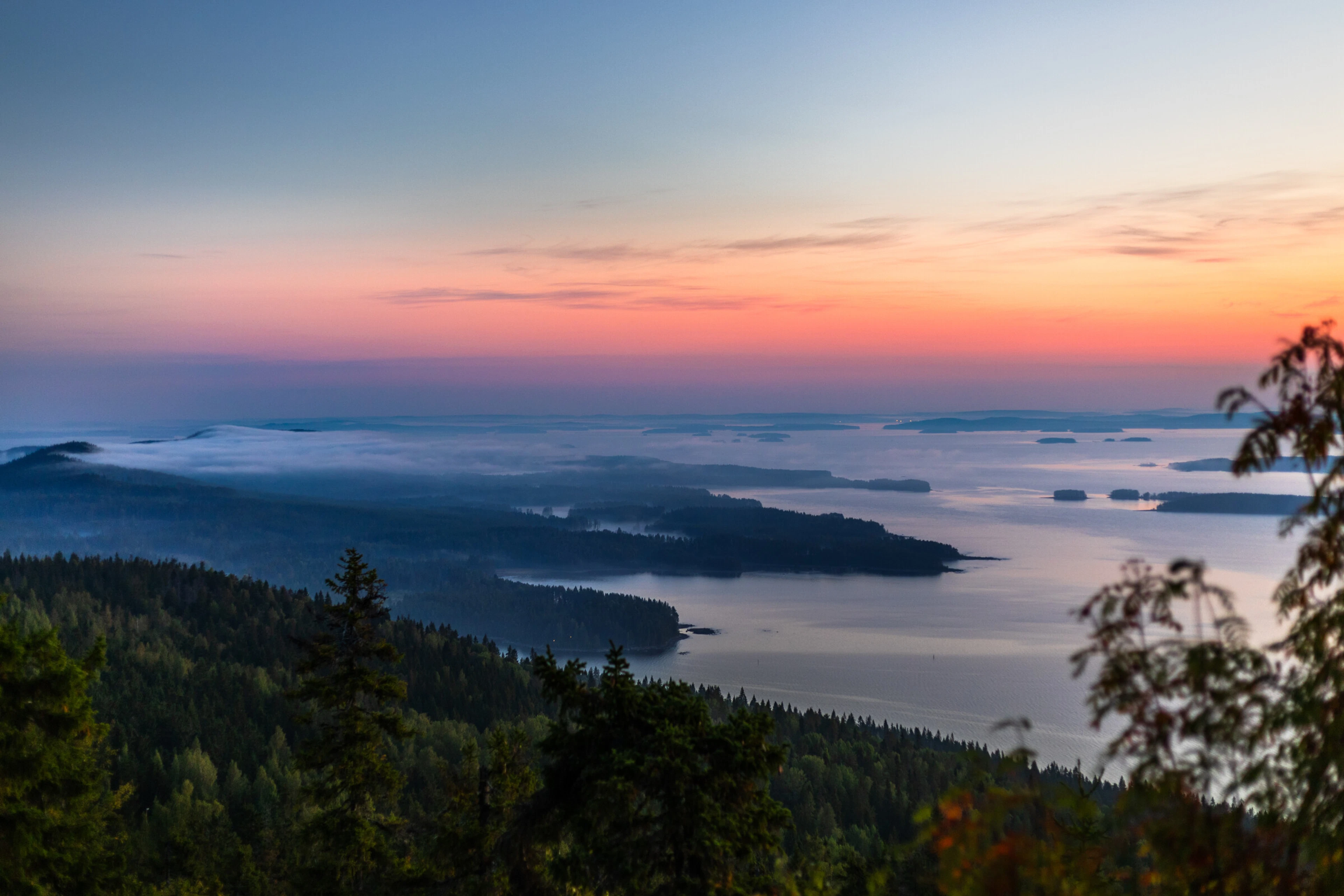 Viewpoint atop a hill overlooking the archipelago with evening sun colouring the sky orange and pink.