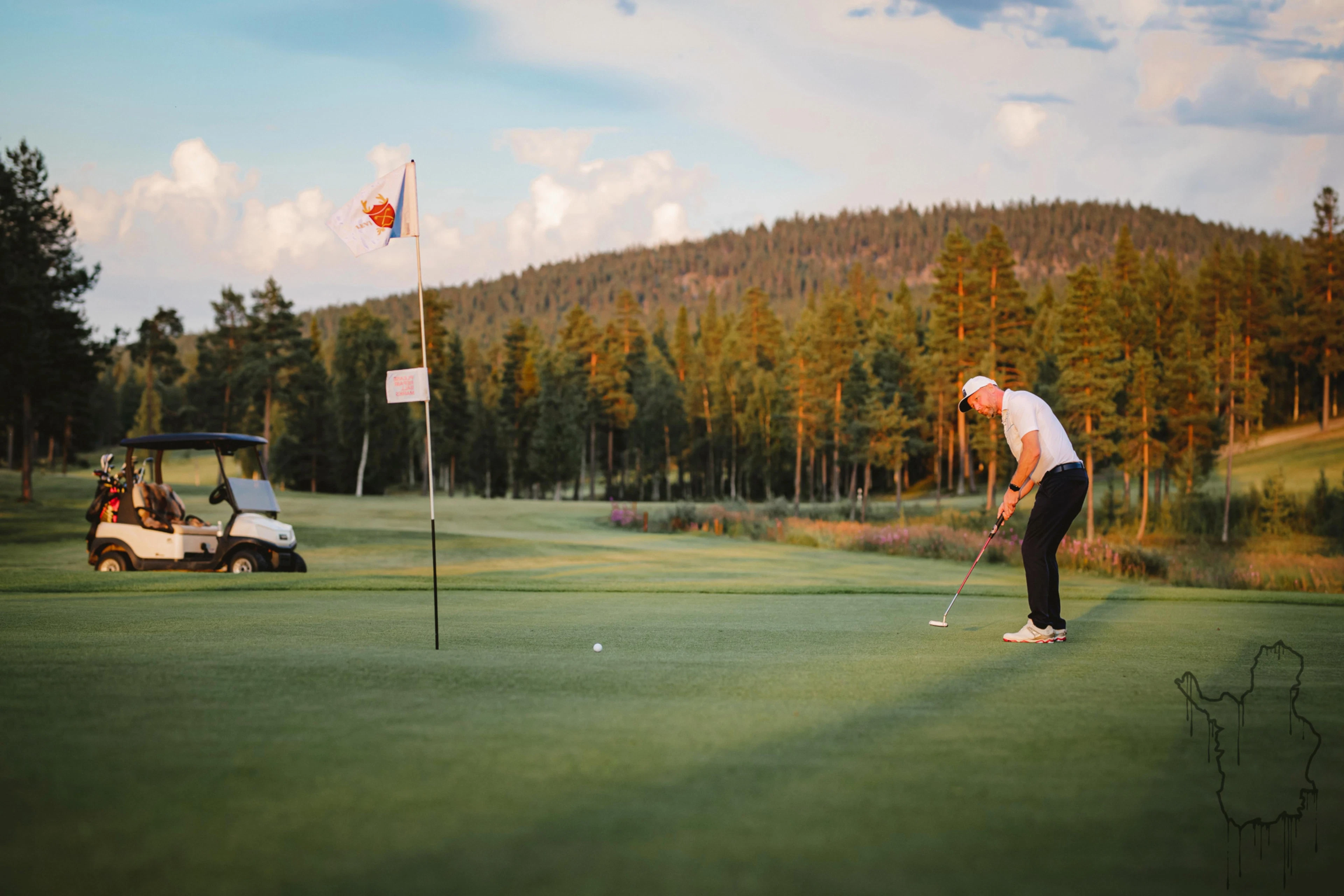 Golfaaja valmistelee lyöntiä tasaisella nurmella, taustalla golfauto ja metsäinen vaara.