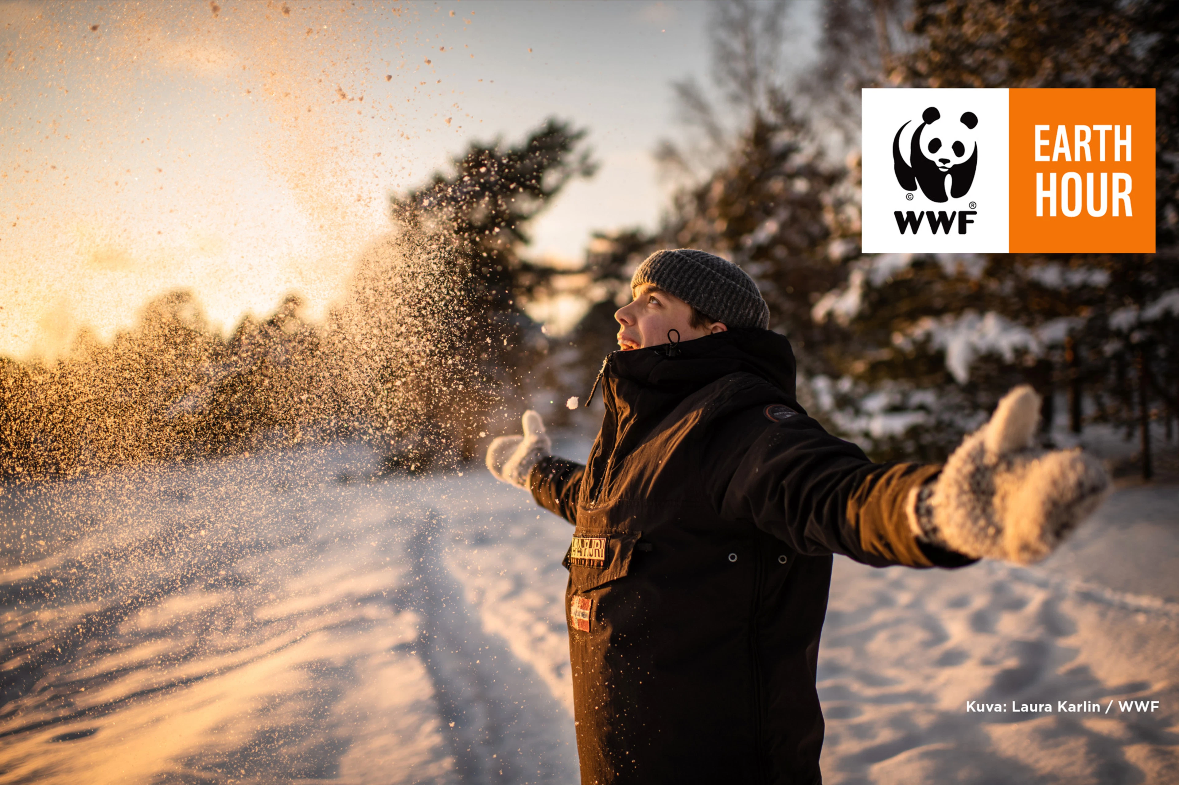 En person kastar snö i luften i solskenet, mitt i en snödriva. I bilden finns WWF:s Earth Hour-logotyp.