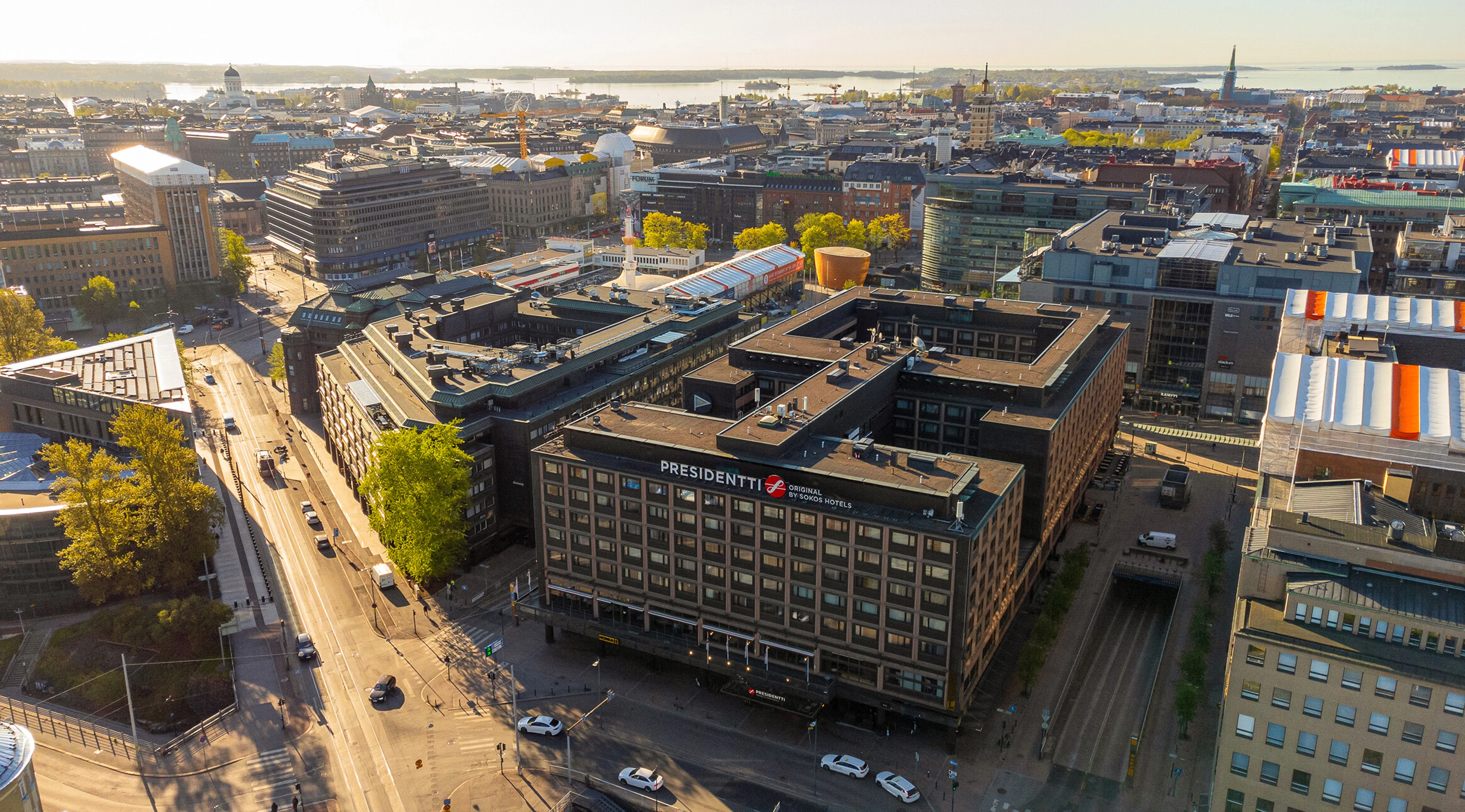 Ilmakuva Helsingin keskustasta, jossa näkyy monikerroksisia rakennuksia, laajoja katuja ja taustalla meren saaria.