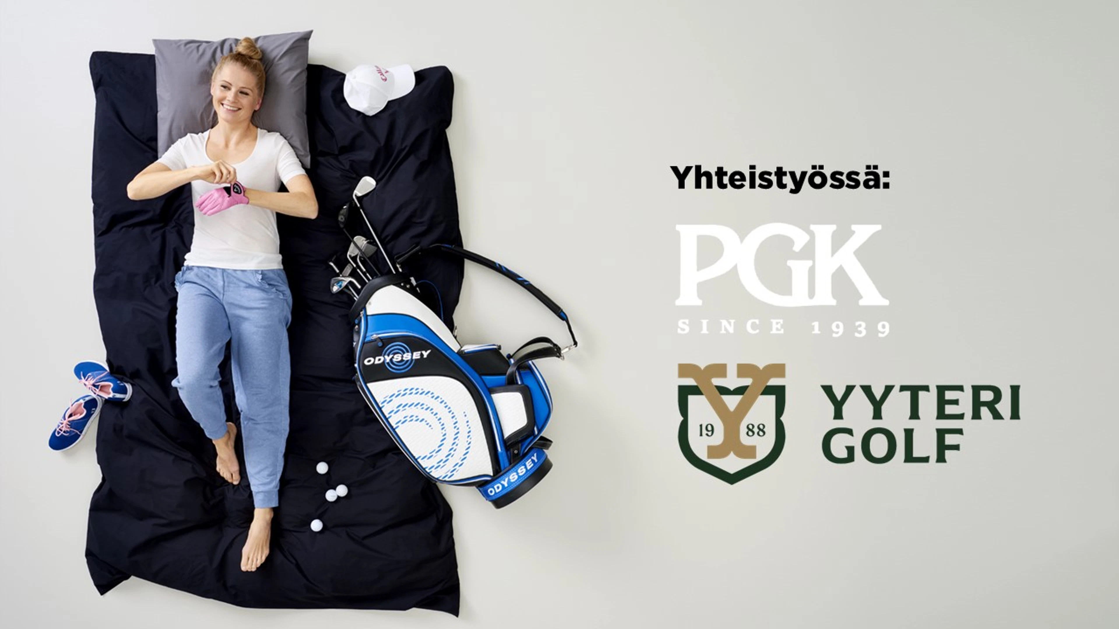 Henkilö makaa mustalla peitolla golf-varusteiden kanssa. Vieressä sinivalkoinen Odyssey-golfbägi ja golfpalloja.