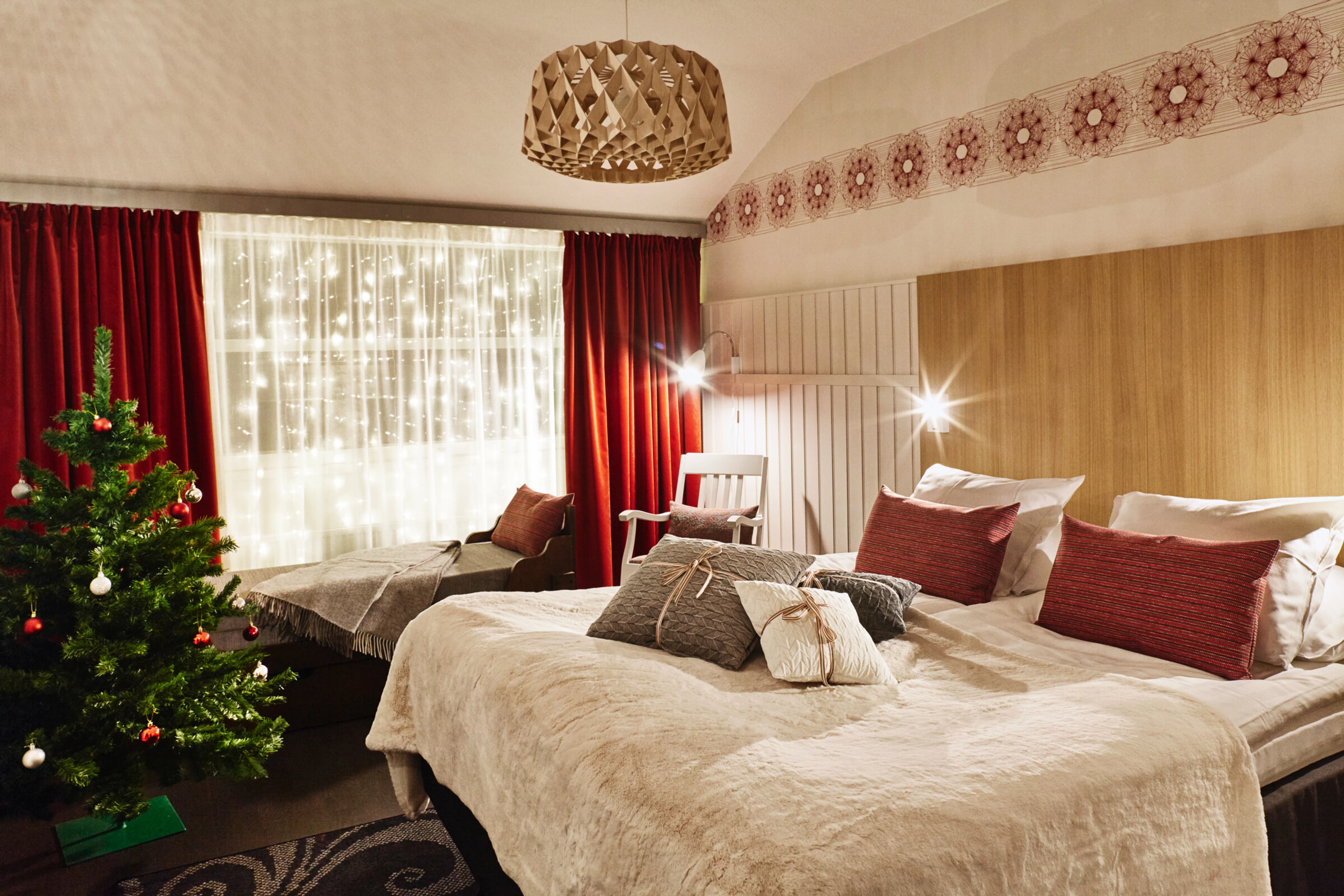 Bedroom with two beds, wooden panelled wall, red curtain and Christmas tree.