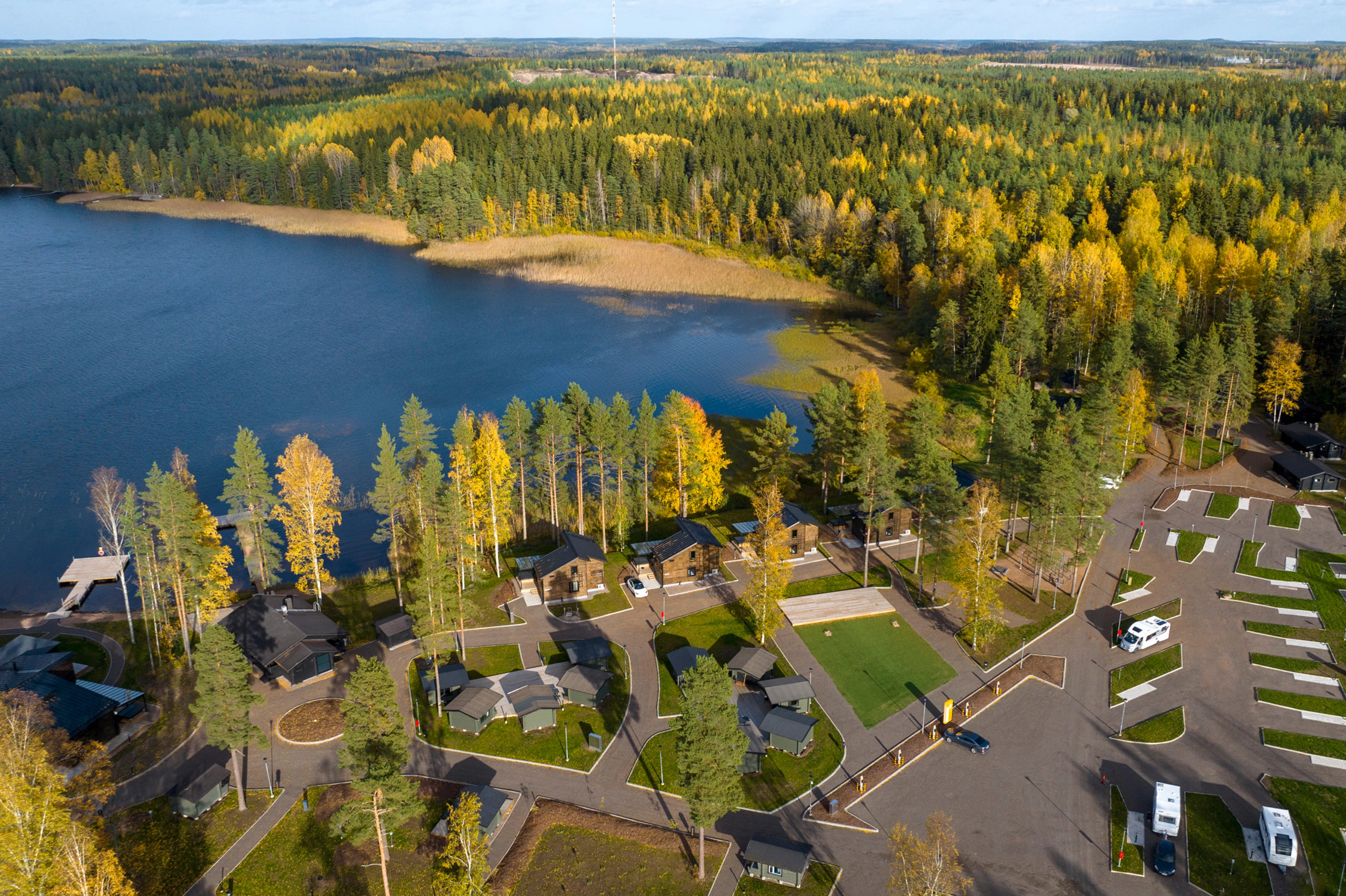 Ilmakuva resortalueesta, jossa näkyy erilaisia huviloita, mökkejä ja camping-alue sekä taustalla järveä ja metsää silmänkantamattomiin.