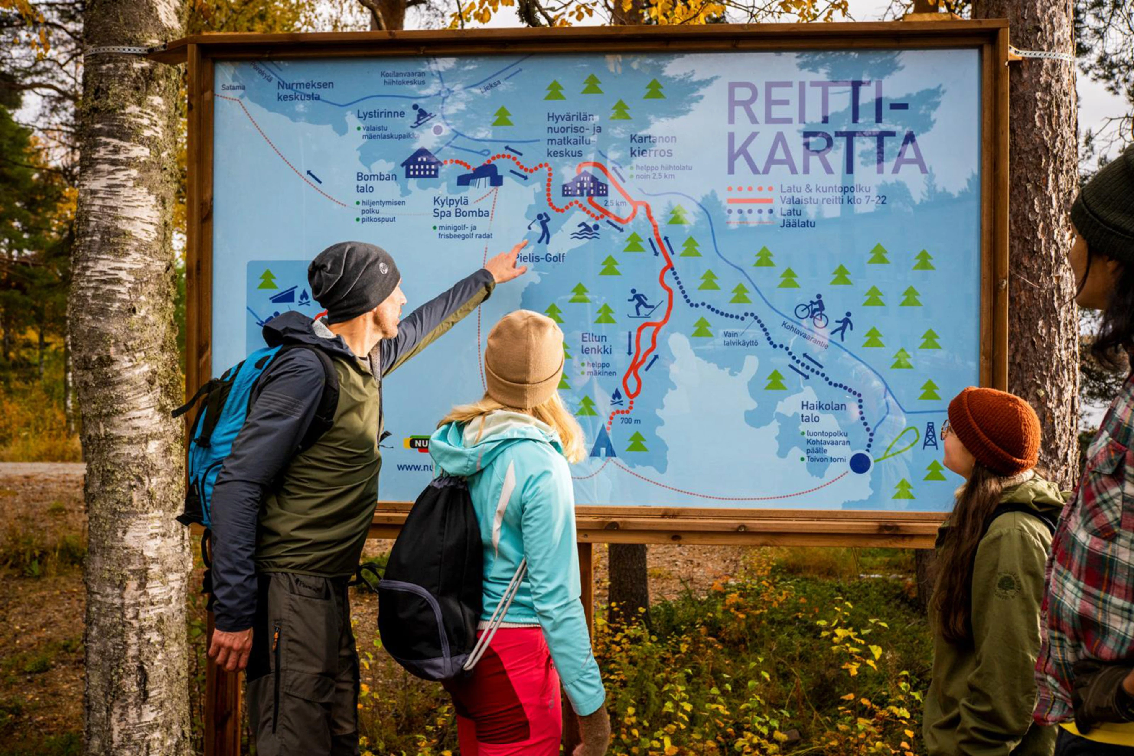 A group of hikers is examining a trail map in nature.