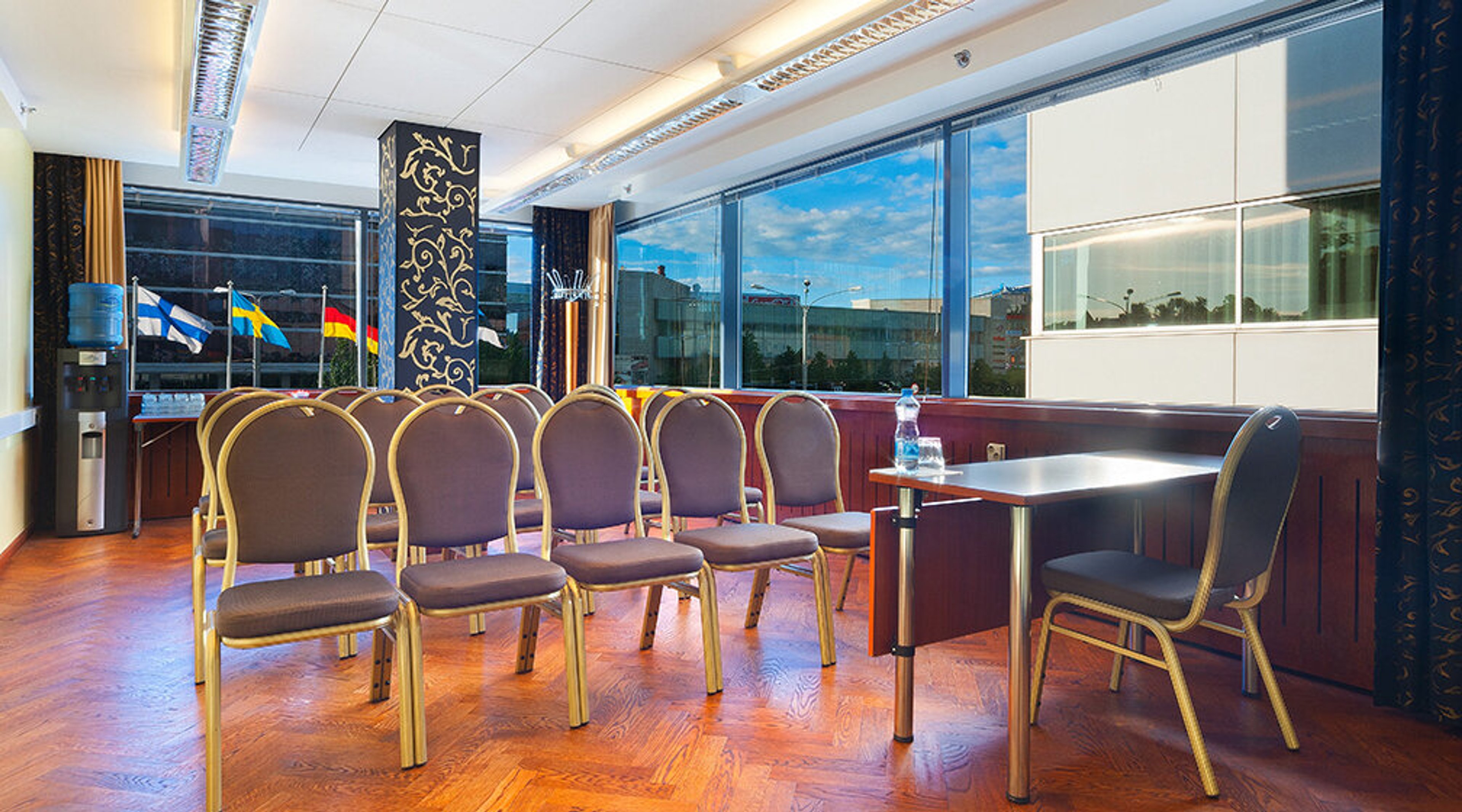 Conference room with wooden parquet floors and purple chairs. Large windows reveal a view with flags and urban landscape outside.