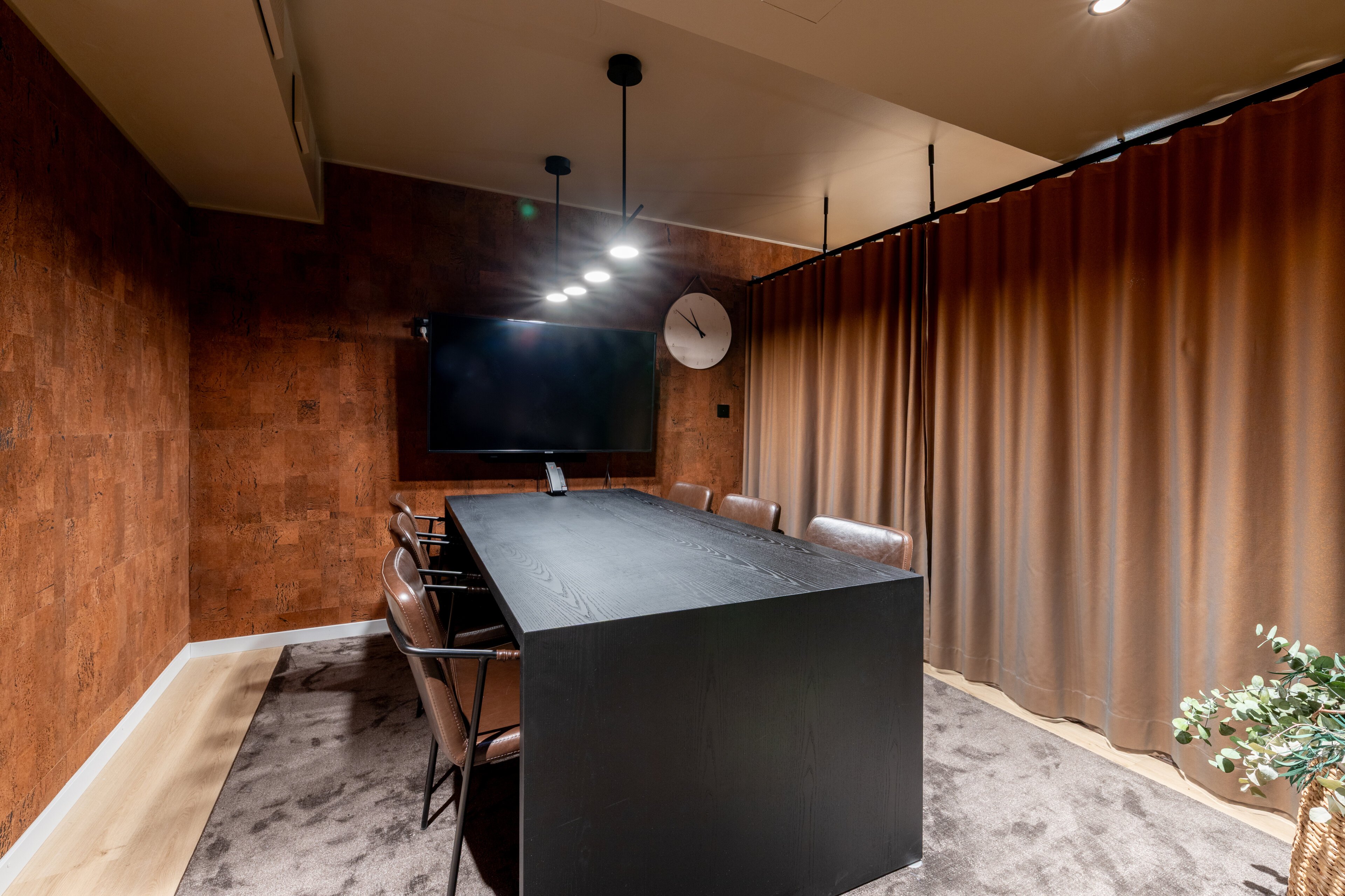 Meeting room with a large black table, cork walls, wall-mounted screen and soft carpet.