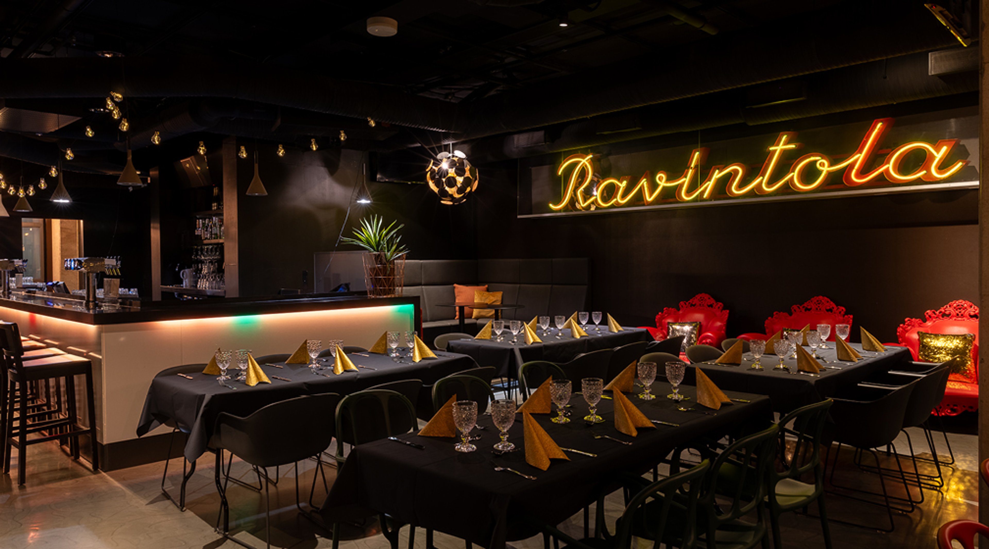 Ravintolan sisätila, jossa mustilla pöytäliinoilla ja kullanvärisillä lautasliinoilla katetut pöydät. Seinällä neon-valokyltti ja taustalla baaritiski.
