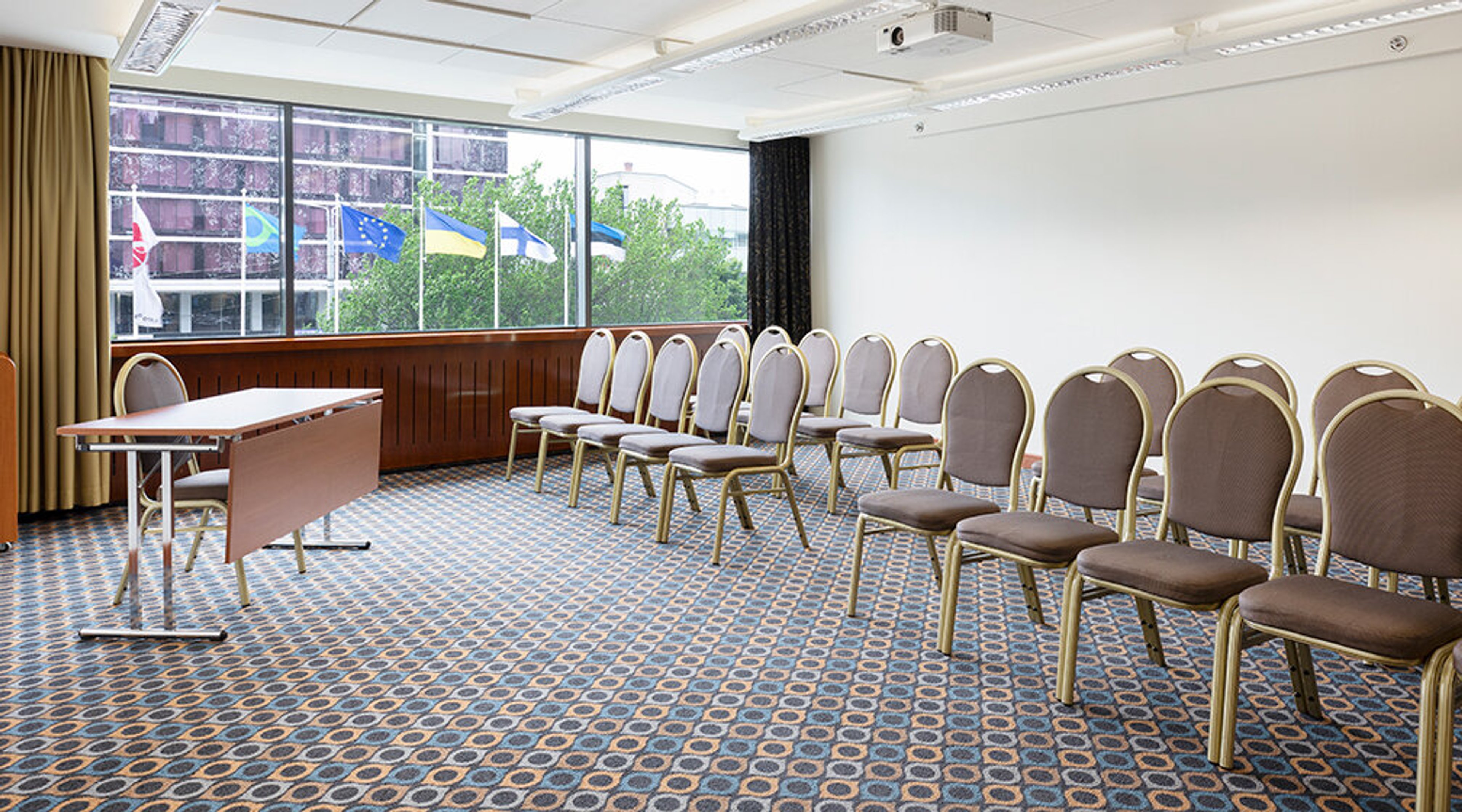 Conference room with chairs arranged in rows, a table and a large window. The room has wall-to-wall carpeting.