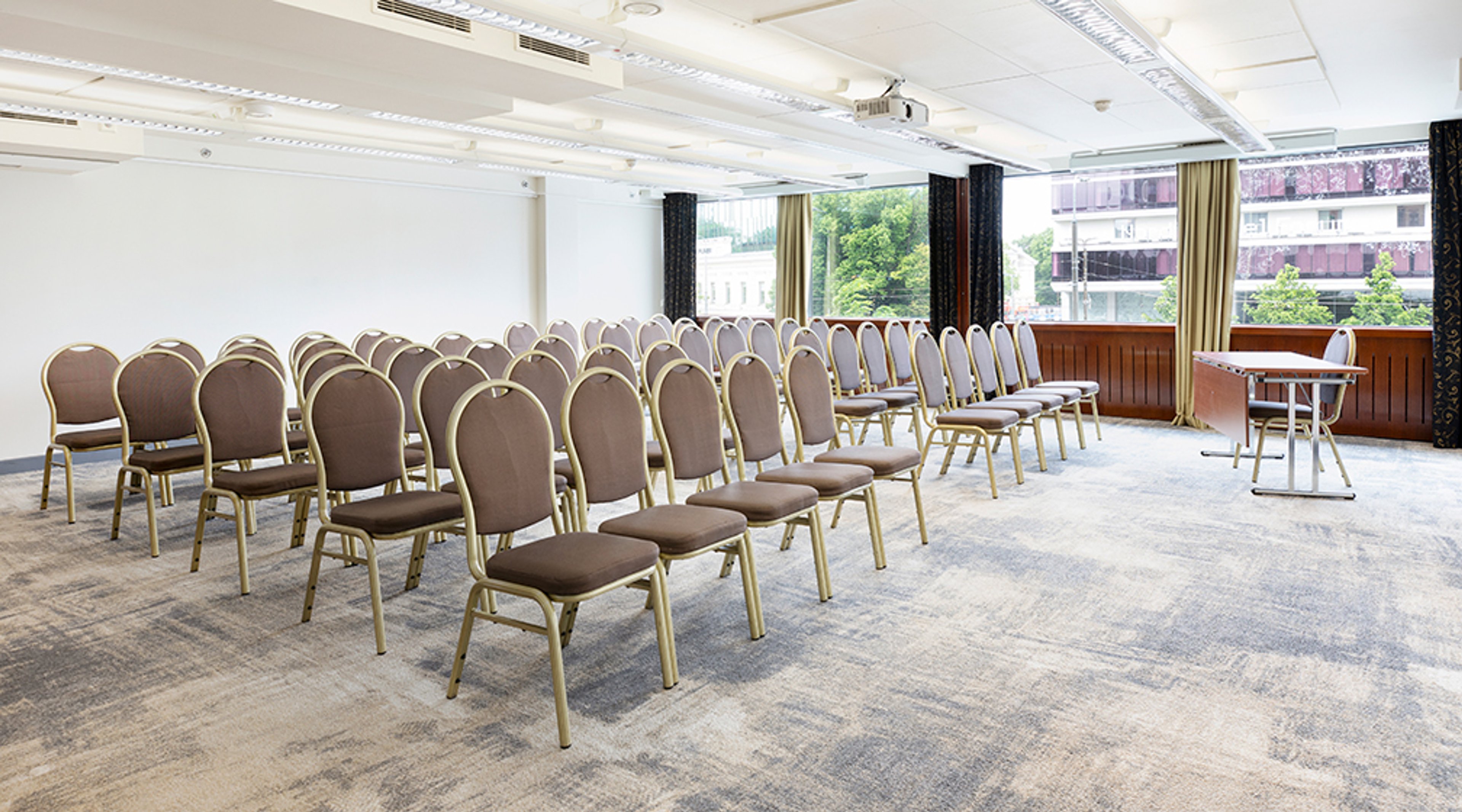 Spacious conference room with rows of upholstered chairs on low-pile carpet. Natural light from large windows.